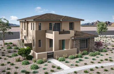 A modern two-story beige house with flat, brown roofing, stone accents, and a small balcony, surrounded by desert landscaping with rocks, shrubs, and distant mountains under a blue sky.