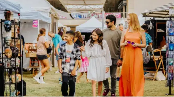 experience-featured A group of four people, including two children and two adults, walk and smile together at an outdoor market with art displays, stalls, and various shoppers in the background.