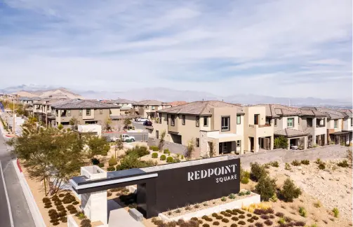 RedpointSquare_Village_featured-image A residential neighborhood with modern two-story houses and landscaped yards, featuring a large entrance sign that reads REDPOINT SQUARE under a partly cloudy sky.