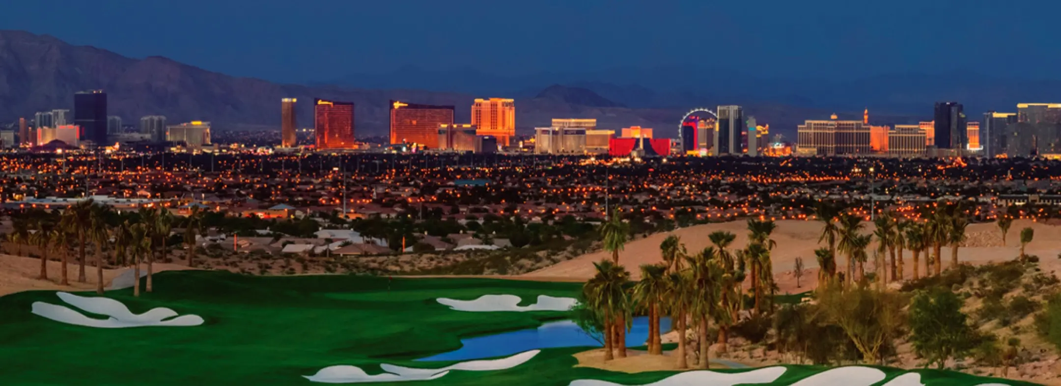 A lush golf course with sand traps and palm trees in the foreground, overlooking the brightly lit Las Vegas Strip skyline at dusk, with mountains in the background.
